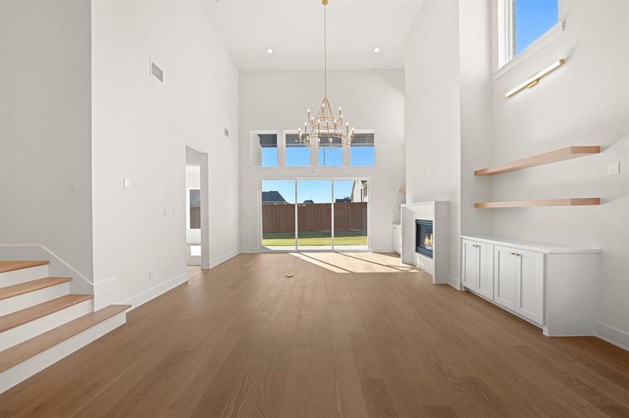 Unfurnished living room with plenty of natural light, light wood-type flooring, a glass covered fireplace, a towering ceiling, and stairway Unfurnished living room with plenty of natural light, light wood-type flooring, a glass covered fireplace, a towering ceiling, and stairway