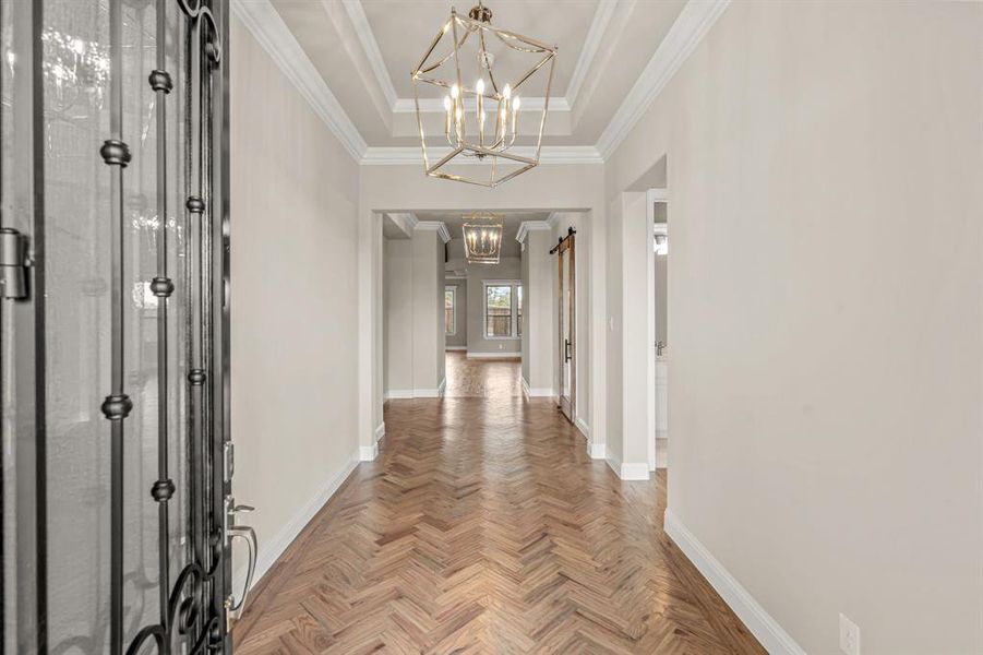 Corridor with a raised ceiling, ornamental molding, and a chandelier