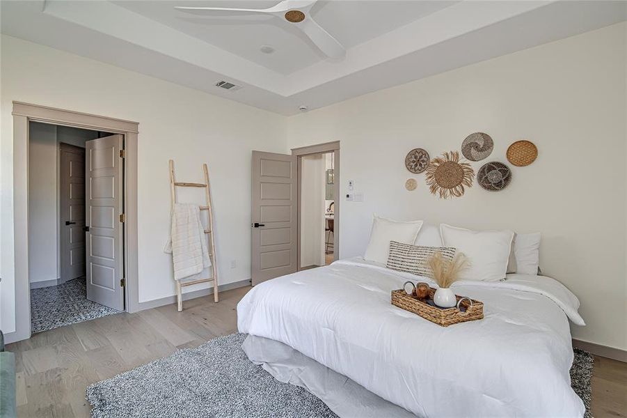 Bedroom with light wood-style floors, a tray ceiling, and ceiling fan