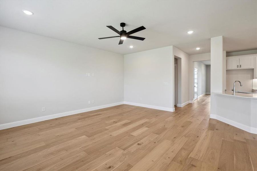 Unfurnished living room featuring a sink, ceiling fan, light wood-style floors, recessed lighting, and baseboards