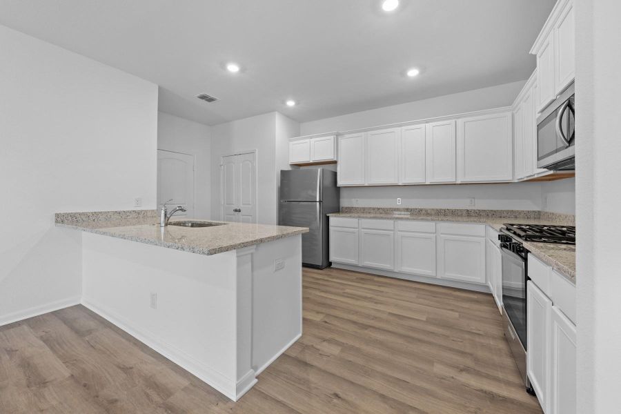 Kitchen featuring appliances with stainless steel finishes, light stone counters, white cabinetry, light wood-style flooring, and recessed lighting