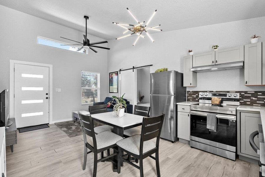 Kitchen featuring a barn door, appliances with stainless steel finishes, a high ceiling, tasteful backsplash, and light wood-style flooring.