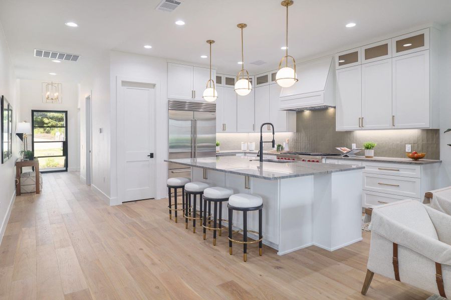 Gourmet kitchen featuring a large central island with seating, stainless steel appliances, a tile backsplash, and white cabinetry