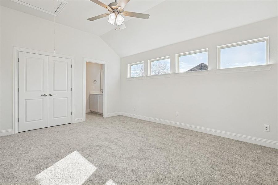 Unfurnished bedroom featuring ceiling fan, lofted ceiling, light carpet, and ensuite bath