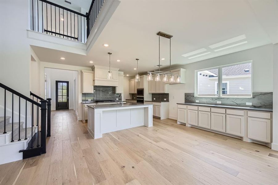 Kitchen featuring decorative backsplash, a sink, black oven, light wood-style flooring, and an island with sink Kitchen featuring decorative backsplash, a sink, black oven, light wood-style flooring, and an island with sink