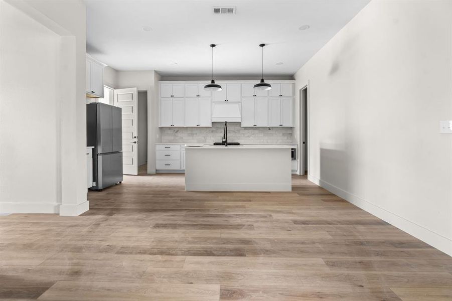 Kitchen with light countertops, white cabinetry, pendant lighting, decorative backsplash, and freestanding refrigerator