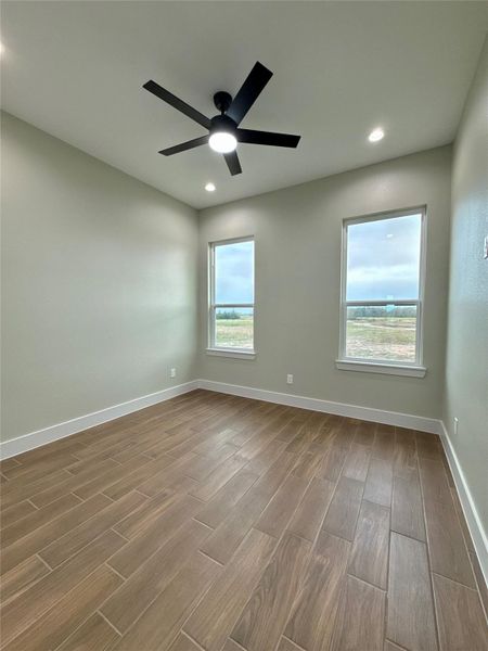 This room features wood-look tile flooring, two large windows offering plenty of natural light, and a modern ceiling fan, creating a bright and airy space.