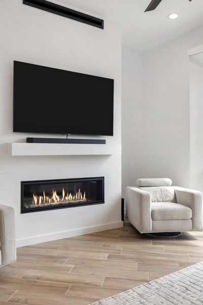 Modern linear fireplace with a white mantel shelf, wood-finish flooring, and recessed ceiling lighting