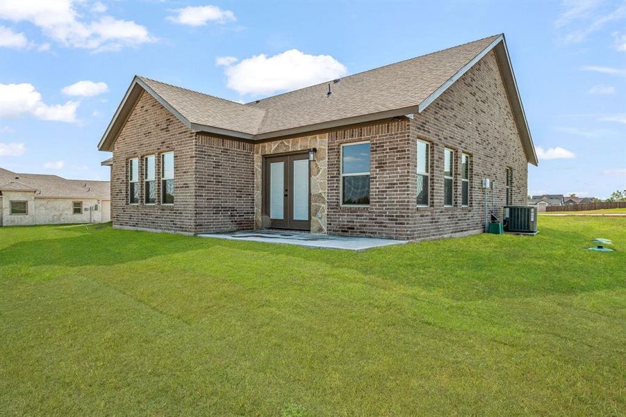Rear view of property featuring brick siding, roof with shingles, a patio, and a lawn