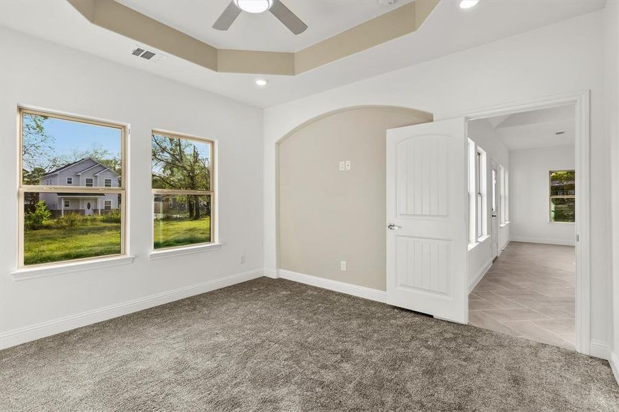 Empty room featuring light carpet, a tray ceiling, and ceiling fan