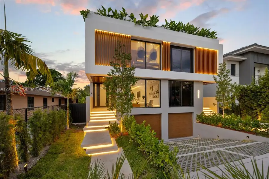 Modern two-story architectural exterior featuring smooth white stucco finish, vertical wood-slat accents, integrated LED stair and facade lighting, large-format glass sliders, and a permeable paver driveway Modern two-story architectural exterior featuring smooth white stucco finish, vertical wood-slat accents, integrated LED stair and facade lighting, large-format glass sliders, and a permeable paver driveway