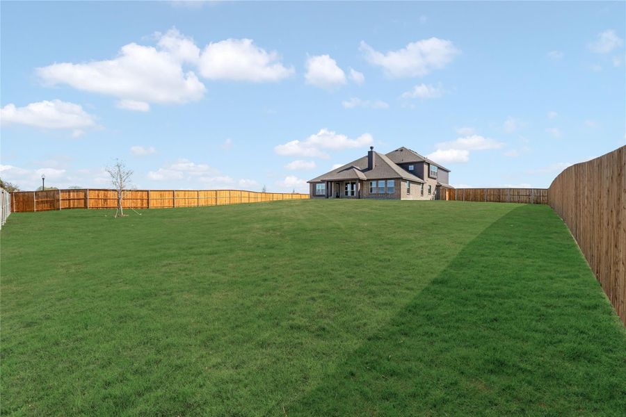 Large backyard with green lawn, wood privacy fence, and two-story brick home in the background Large backyard with green lawn, wood privacy fence, and two-story brick home in the background
