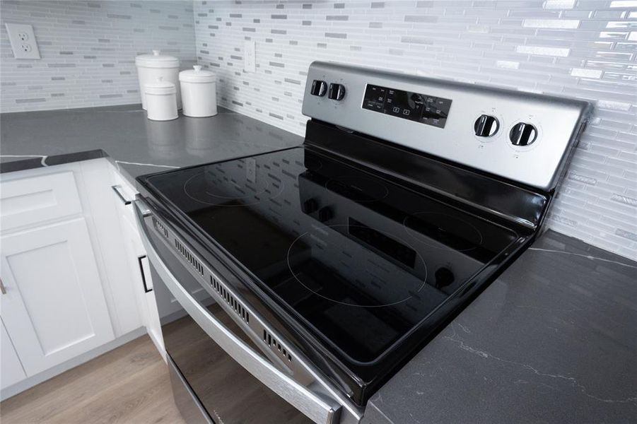 Kitchen with backsplash, light hardwood / wood-style floors, white cabinetry, and stainless steel electric stove