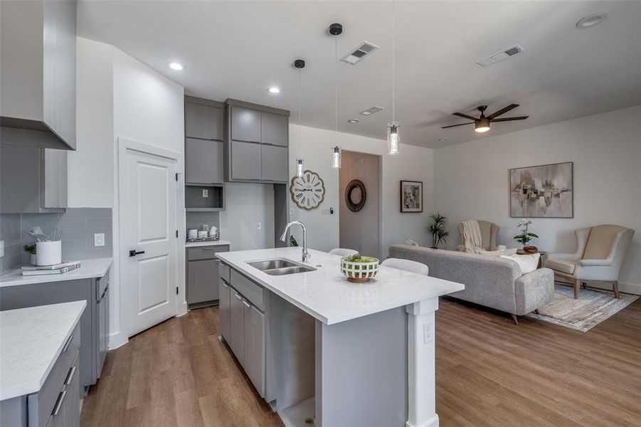 Kitchen featuring light hardwood / wood-style floors, gray cabinetry, an island with sink, sink, and ceiling fan