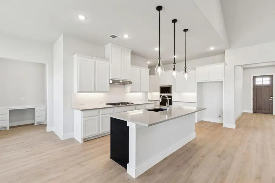 Kitchen featuring white cabinets, a kitchen island with sink, decorative backsplash, pendant lighting, and light wood-style flooring