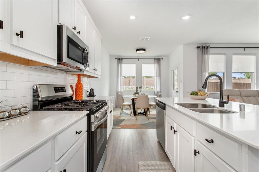 The kitchen features white cabinetry, white countertops, a stainless steel microwave, and a black and stainless steel range