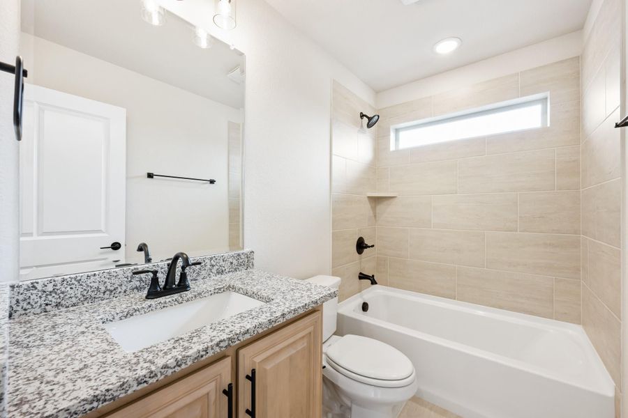 Bathroom with granite vanity, wood cabinets, tub-shower combo with beige tile, and black fixtures Bathroom with granite vanity, wood cabinets, tub-shower combo with beige tile, and black fixtures