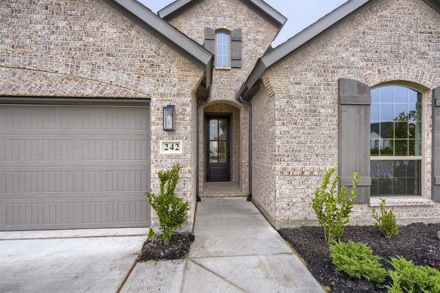 Brick exterior facade with an arched entry, a paneled garage door, and a prominent arched window featuring decorative shutters