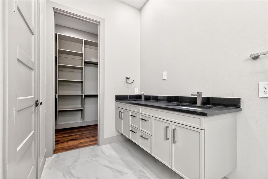 Bathroom with double vanity, light marble finish flooring, and a walk in closet Bathroom with double vanity, light marble finish flooring, and a walk in closet