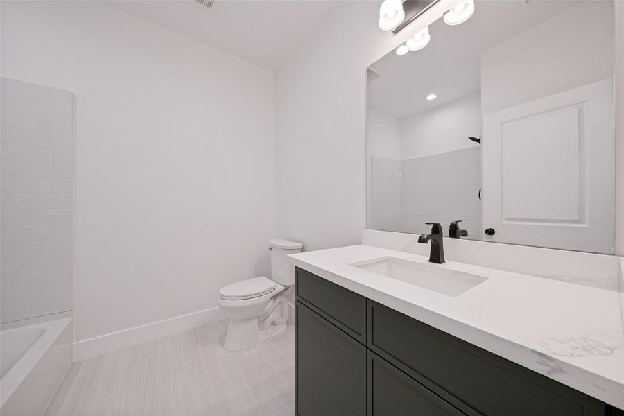 A well-appointed bathroom features a dark vanity cabinet topped with a pristine white counter, alongside a sleek toilet and a bathtub. A well-appointed bathroom features a dark vanity cabinet topped with a pristine white counter, alongside a sleek toilet and a bathtub.