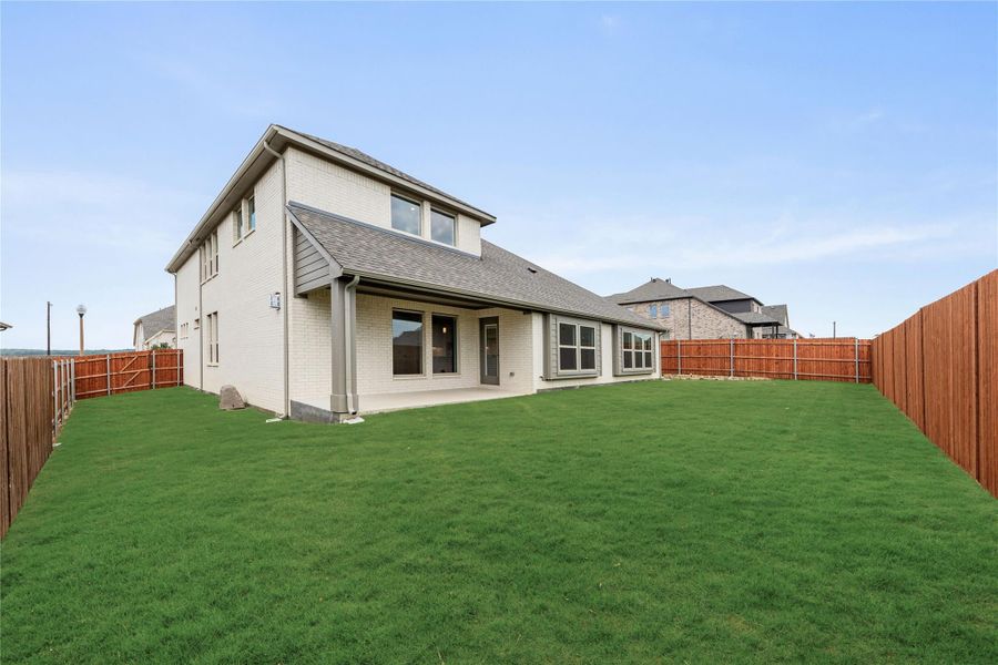Two-story brick home with covered back patio, large grassy yard, and wood privacy fence