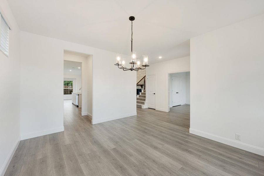 Empty dining room with black chandelier, gray wood floors, and open view to kitchen and staircase