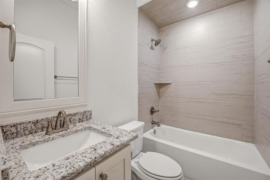 Bathroom featuring a vanity with a granite countertop, a bathtub with a tiled surround, and a mirror