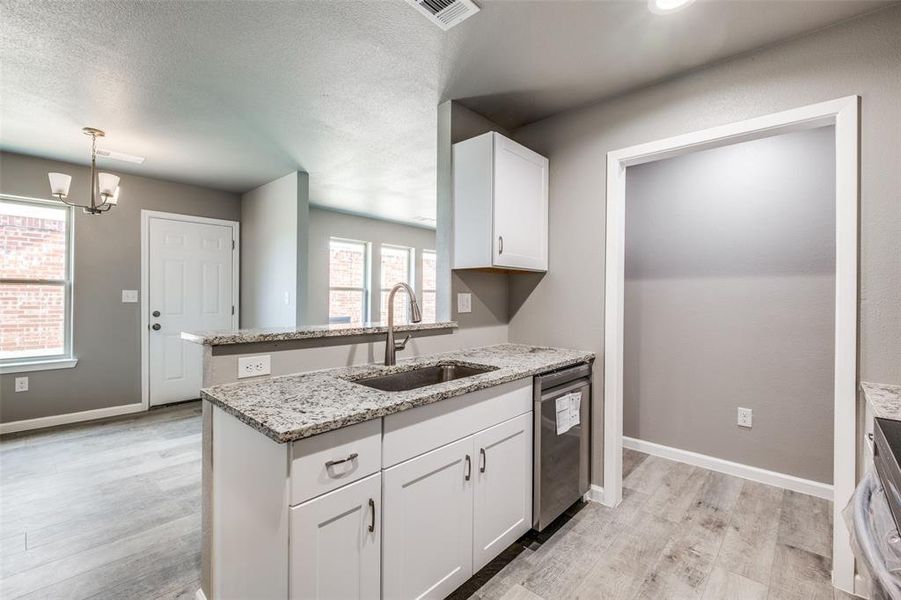 Kitchen featuring white cabinets, light stone countertops, sink, stainless steel dishwasher, and light hardwood / wood-style floors