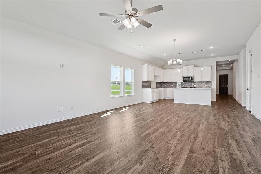 Unfurnished living room with ceiling fan with notable chandelier and dark hardwood / wood-style flooring