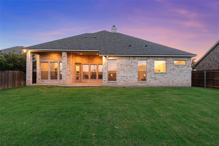 Stone and brick rear elevation with covered patio at dusk, backing up to open land. Stone and brick rear elevation with covered patio at dusk, backing up to open land.
