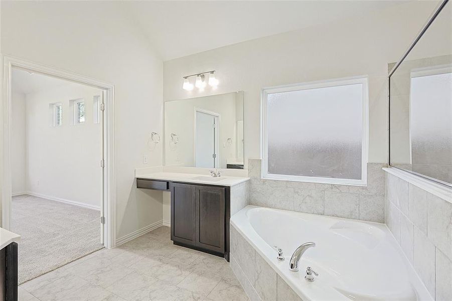 Bathroom with vanity, tiled bath, and vaulted ceiling