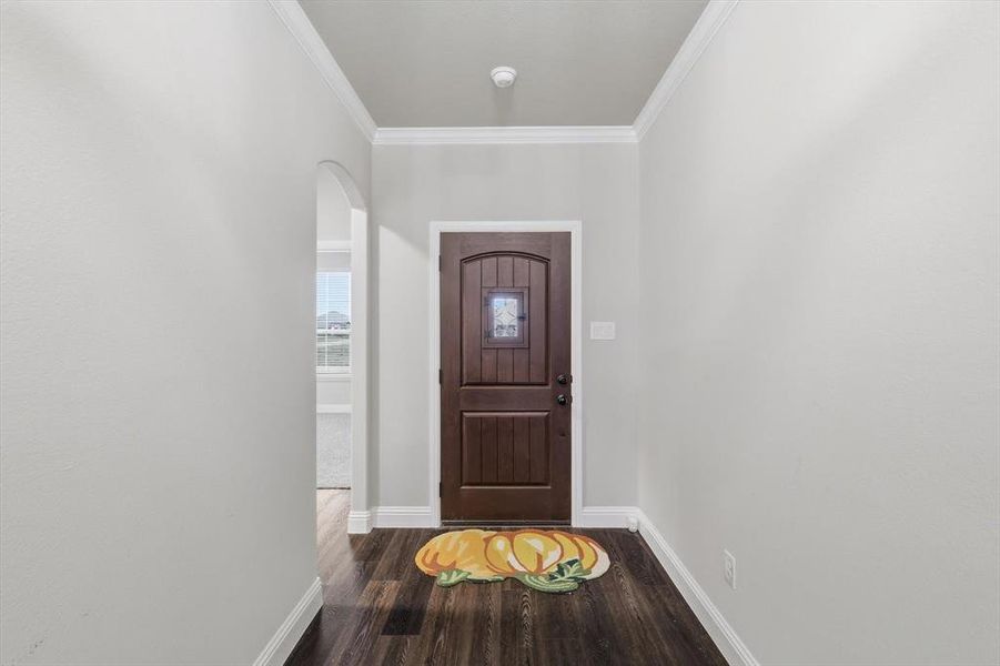 Foyer with arched walkways, crown molding, and dark wood-style flooring
