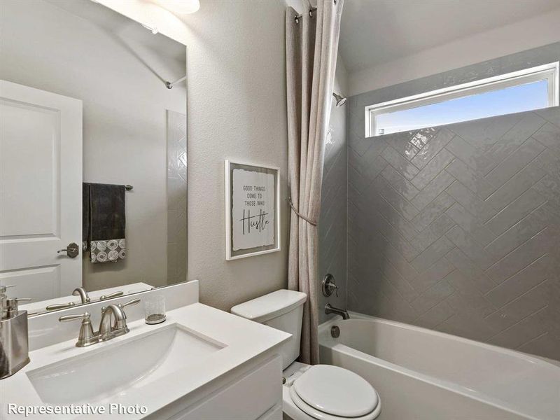Bathroom featuring a white vanity with an integrated sink, a white toilet, and a bathtub with a herringbone-patterned tiled surround