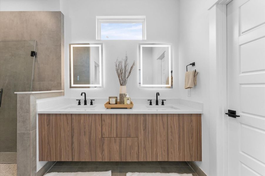 The luxurious primary ensuite features sleek modern finishes, a glass-enclosed shower with stylish tile, and a double-sink vanity topped with quartz countertops, complemented by two contemporary mirrors and lighting fixtures, creating a bright, elegant, and functional retreat.