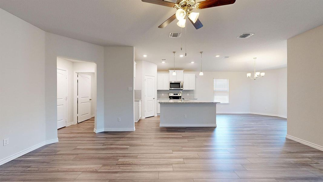 Kitchen featuring open floor plan, ceiling fan, a center island with sink, white cabinets, and light wood-style floors Kitchen featuring open floor plan, ceiling fan, a center island with sink, white cabinets, and light wood-style floors