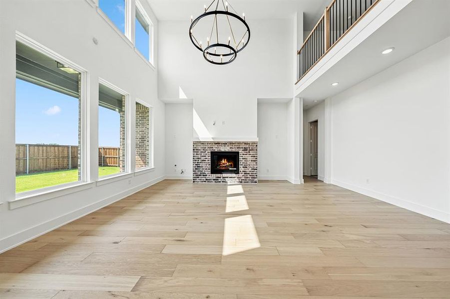 Unfurnished living room featuring a fireplace, light wood finished floors, a towering ceiling, and a chandelier