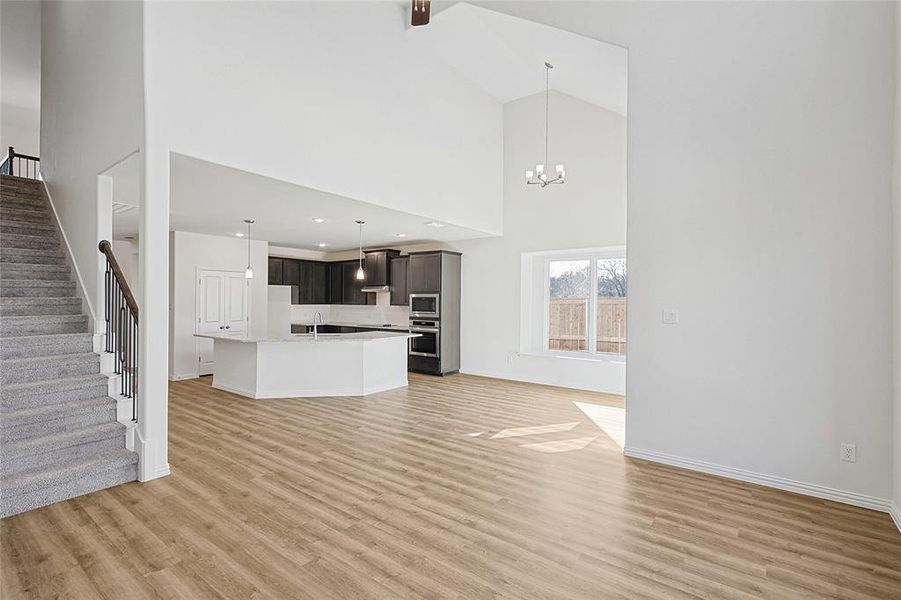 Unfurnished living room with sink, a towering ceiling, light hardwood / wood-style flooring, and an inviting chandelier