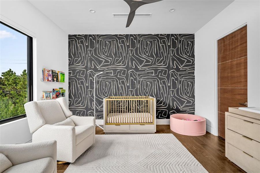 This serene secondary bedroom features a striking accent wall with bold, Kelly Wearstler wallpaper, adding a playful yet sophisticated element to the space. The large window invites natural light, creating a bright and airy atmosphere throughout the room.