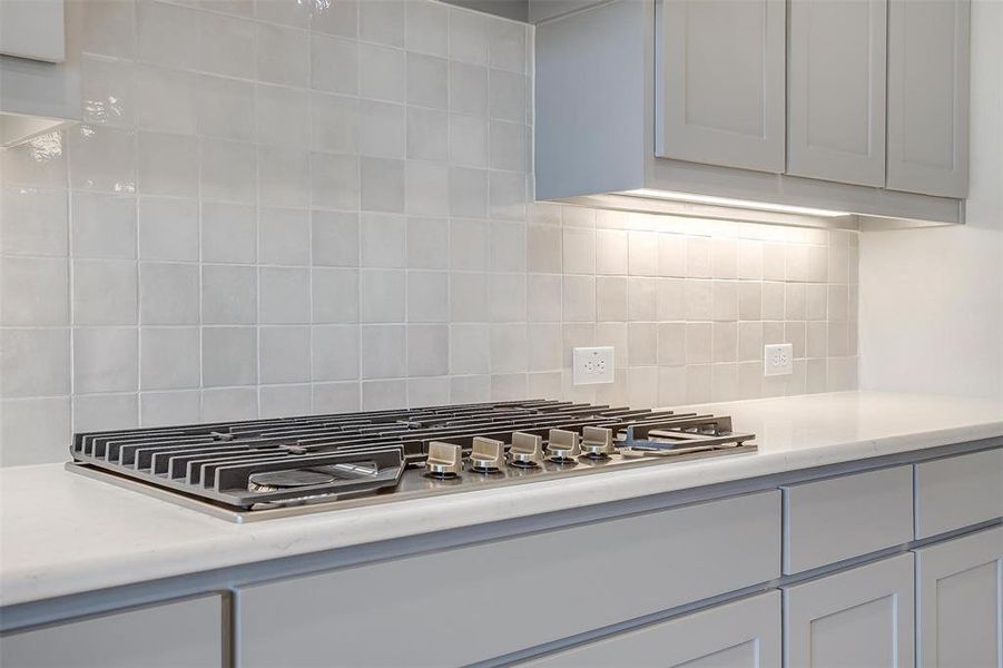 Kitchen with stainless steel gas stovetop and decorative backsplash