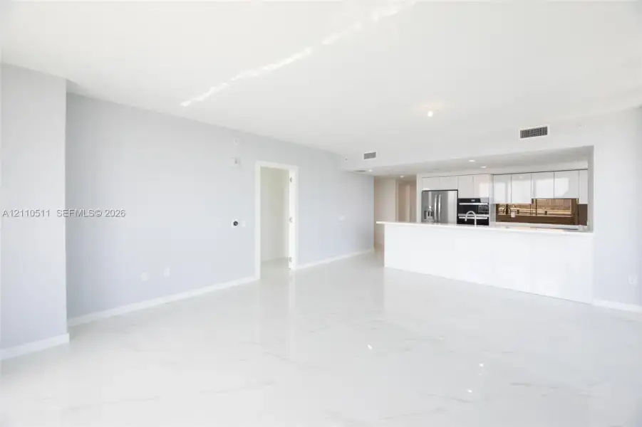 Open-concept interior featuring large-format tile flooring, white gloss cabinetry, a peninsula with a waterfall-edge countertop, and stainless steel built-in appliances
