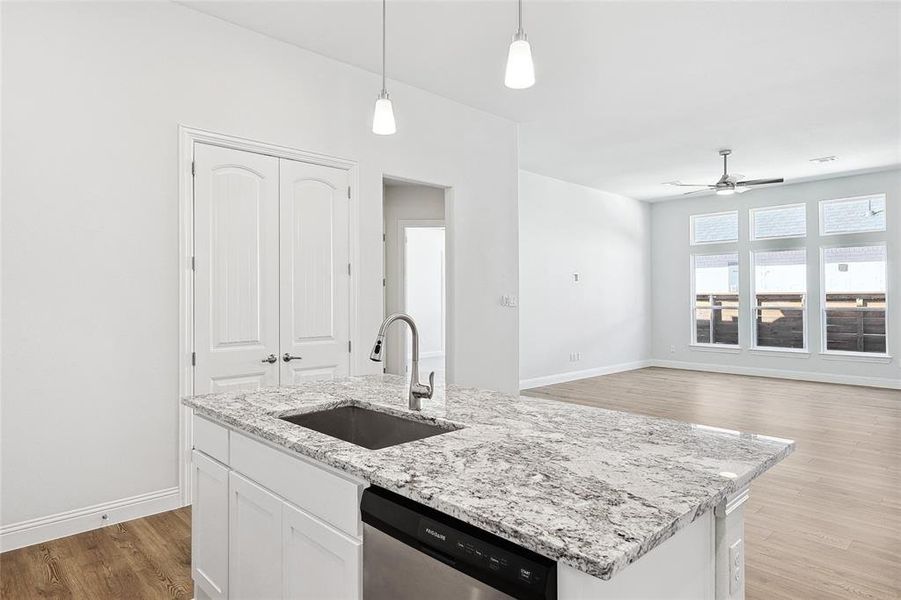Kitchen featuring light wood finished floors, dishwasher, white cabinets, light stone countertops, and pendant lighting