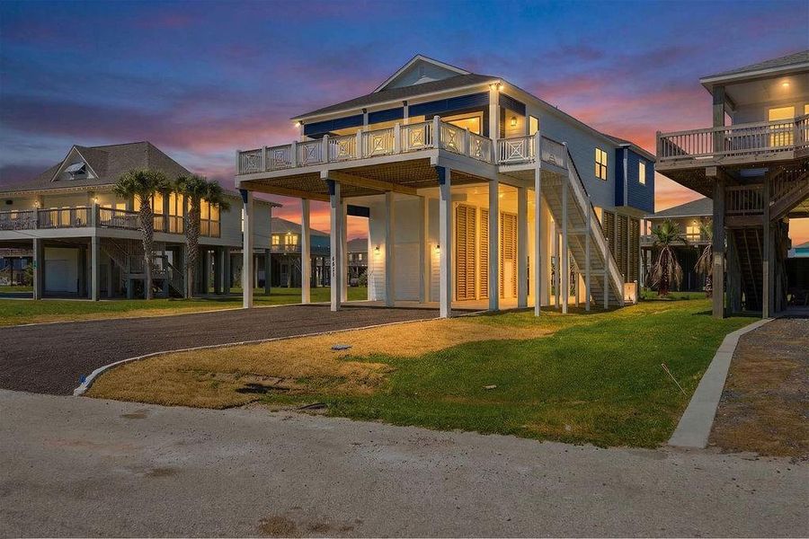 This elevated coastal home features a modern design with a spacious upper deck, offering stunning sunset views. It has an open driveway, a well-maintained lawn, and is situated in a serene neighborhood. Perfect for enjoying beachside living with a touch of elegance.