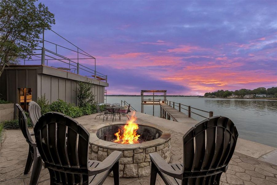 Waterside patio featuring a stone-clad fire pit, stamped concrete, and a private dock leading to the water