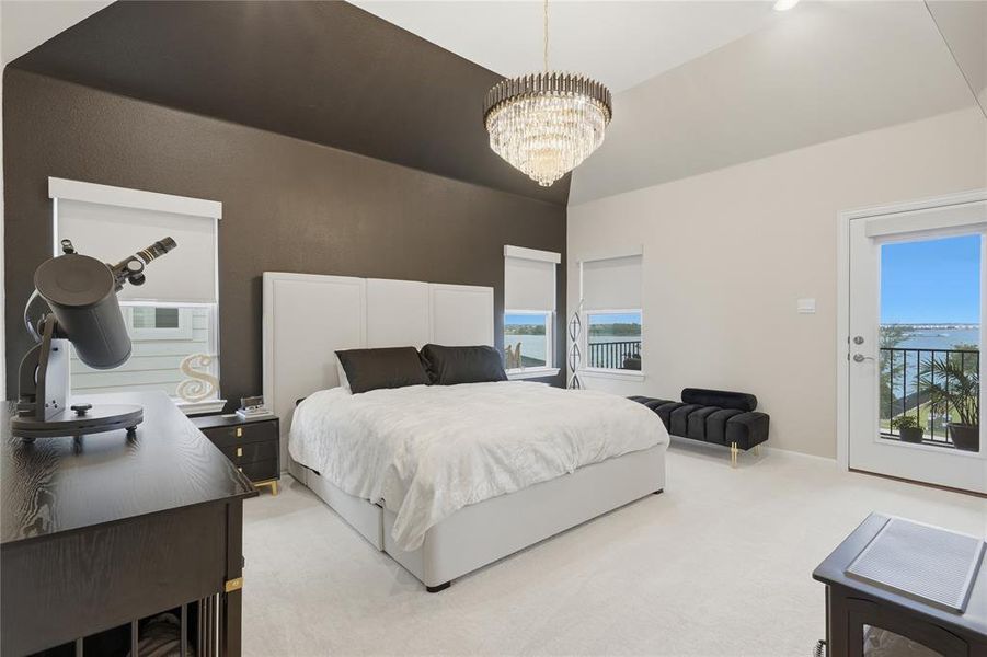 Vaulted ceiling bedroom featuring a chandelier, private balcony access, carpeted flooring, and multiple windows with water scenery Vaulted ceiling bedroom featuring a chandelier, private balcony access, carpeted flooring, and multiple windows with water scenery