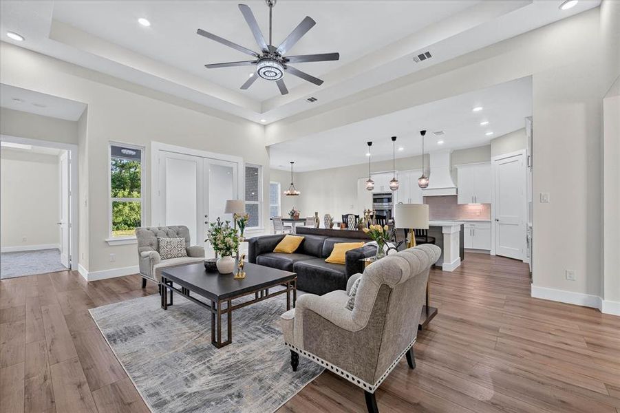 Open-concept living space featuring wood-finish flooring, a tray ceiling with recessed lighting, and a contemporary ceiling fan Open-concept living space featuring wood-finish flooring, a tray ceiling with recessed lighting, and a contemporary ceiling fan