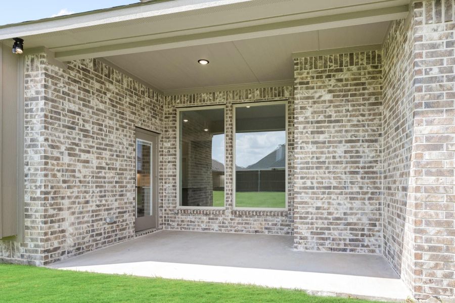 Covered back patio with brick exterior, concrete floor, large window, and back door leading to green yard