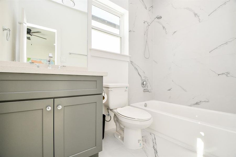 This modern bathroom features elegant marble-style tile, a sleek vanity with ample storage, and a combined shower and bathtub under a bright window.