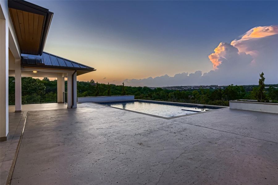 This property features an expansive outdoor patio, an infinity-edge pool, and a covered veranda with distant views of green landscaping and a cityscape