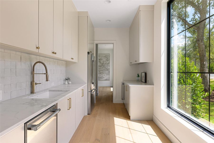 A stylish wet bar with geometric tile backsplash and gleaming marble countertops offers effortless entertaining.