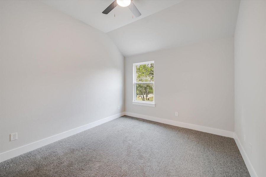 Carpeted empty room with a ceiling fan, vaulted ceiling, and baseboards